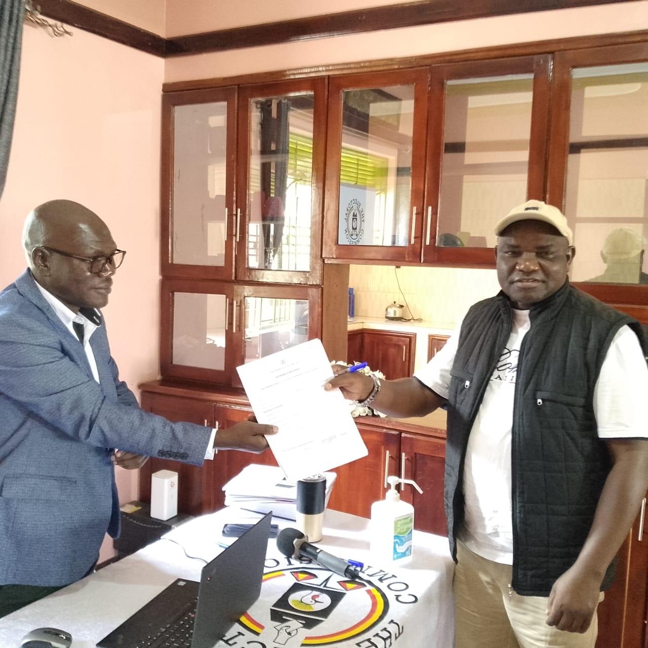 Emmanuel Ogwang, Zombo's Returning Officer (L), hands over nomination forms to MP Lawrence Songa Biyika (R), at the Electoral Commission offices in Paidha Town Council on September 11, 2025.